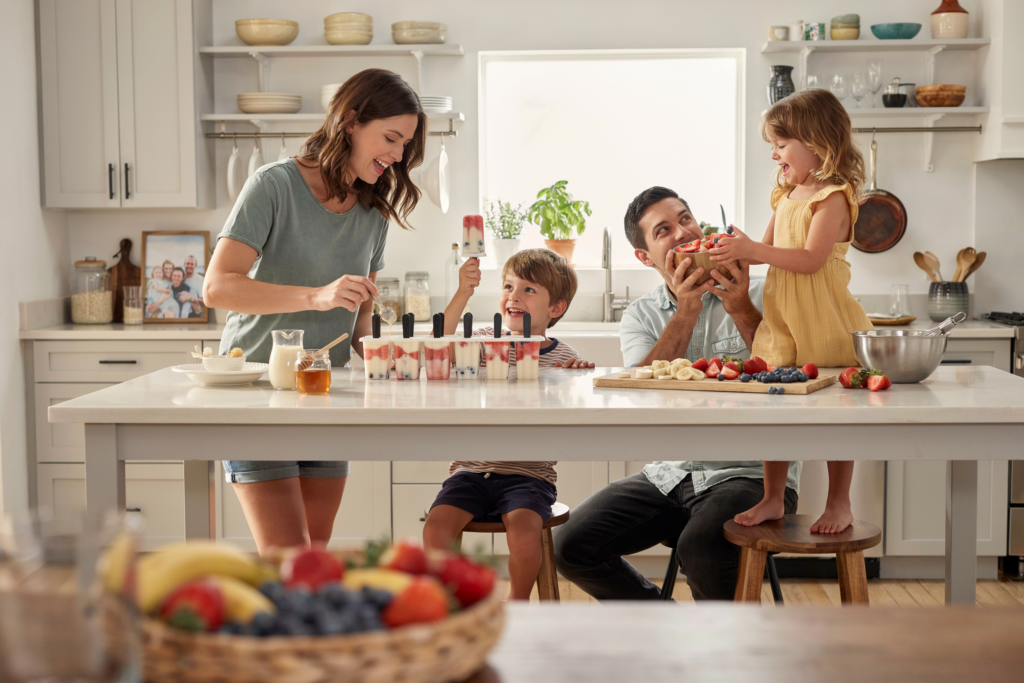 Kinder und Eltern bereiten gemeinsam selbstgemachtes Eis mit frischen Früchten zu und verbringen kreative Familienzeit in der Küche.