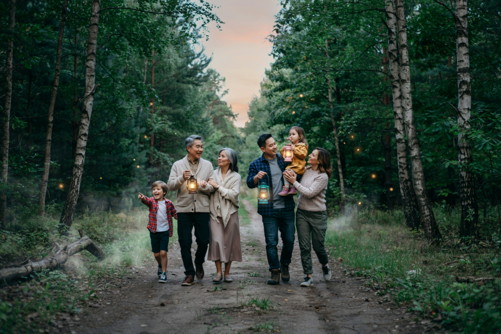 Familie mit Kindern und Großeltern unternimmt gemeinsam eine stimmungsvolle Nachtwanderung mit Laternen bei Dämmerung.