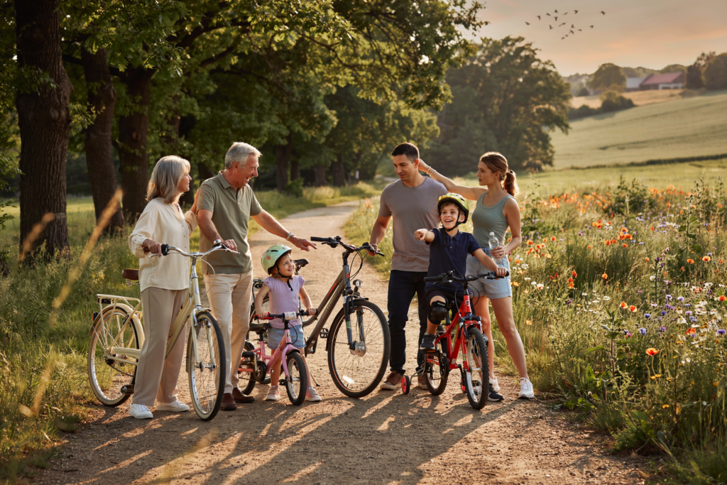 Familie mit Kindern und Großeltern unternimmt gemeinsam eine entspannte Radtour durch eine sommerliche Landschaft.